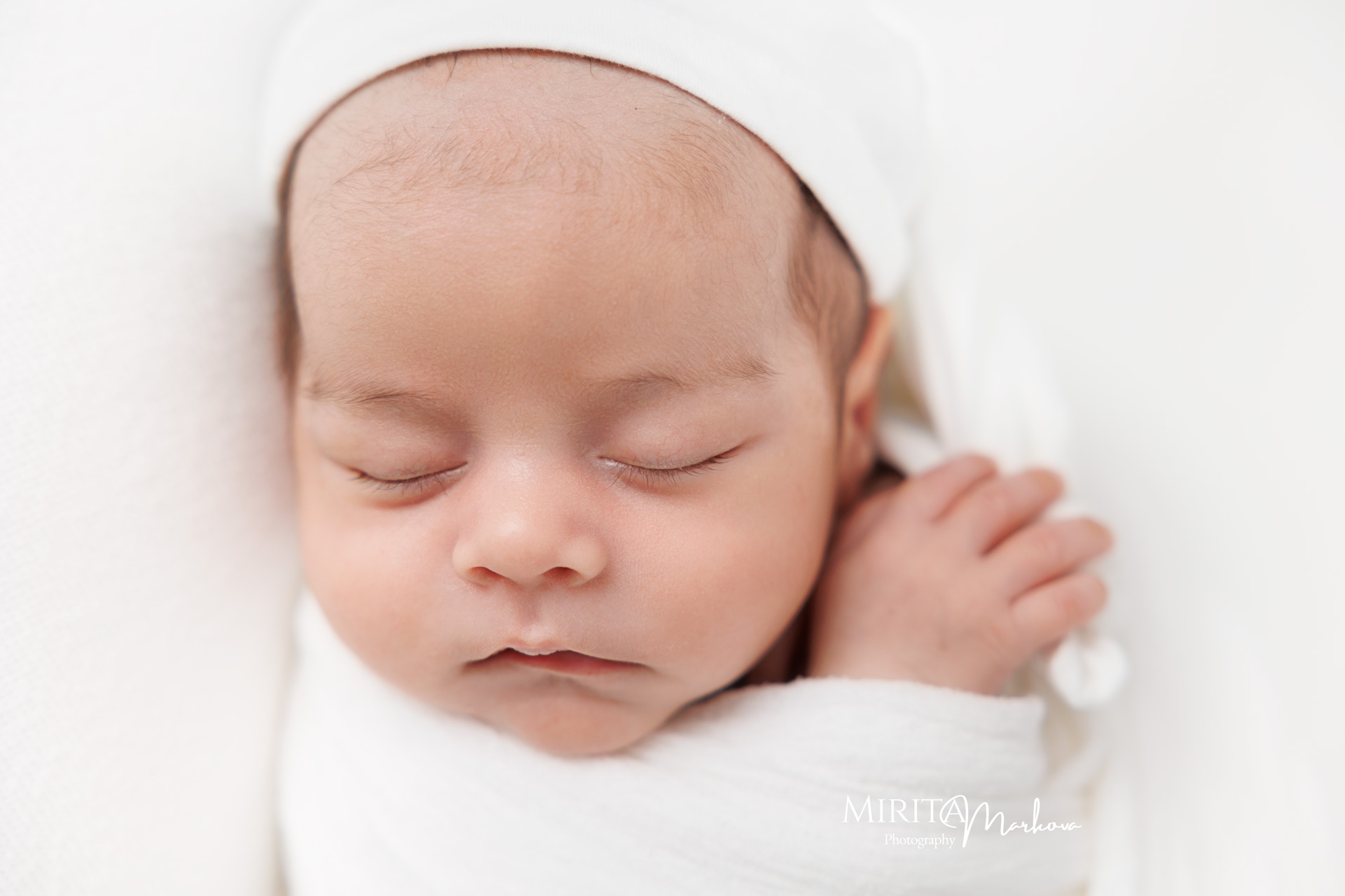 Спящо новородено бебе с бяла шапчица.