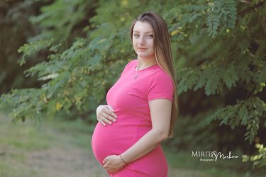 Красива бременна дама сред зеленина в парка.